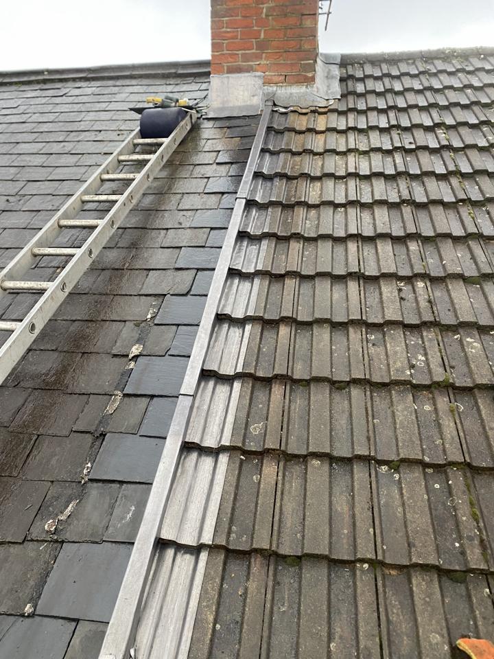 Metal flashing where a slate roof meets a tiled roof beside a chimney